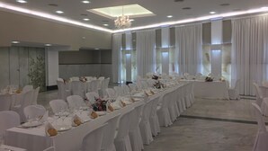 Une salle de banquet avec de longues tables, des chaises blanches et un lustre.