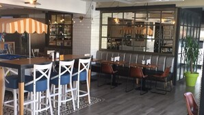Un vaste espace dédié à la salle à manger, avec une longue table en bois et de nombreuses chaises, un coin bar avec des tabourets, et une grande fenêtre qui laisse entrer la lumière naturelle.