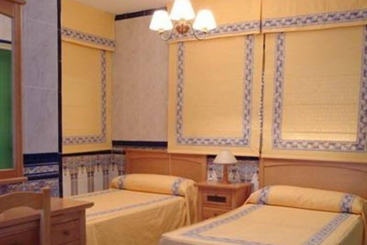 A hotel room with two single beds, a wooden desk, a nightstand, and a chandelier.