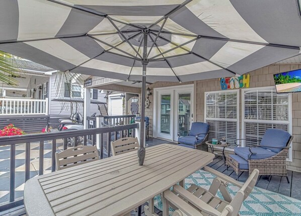 Une terrasse extérieure avec une table et des chaises, un grand parasol et une vue sur la rue.