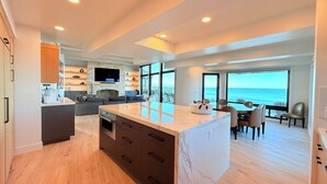 Una cocina moderna con una isla grande, un comedor con vistas al océano y una zona de estar acogedora con chimenea.