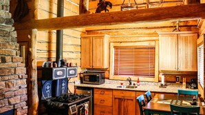 A rustic kitchen with wooden cabinets, a stove, a microwave, and a hanging light fixture.