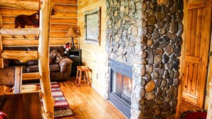 A cozy log cabin interior with a stone fireplace, wooden walls, and a leather sofa.