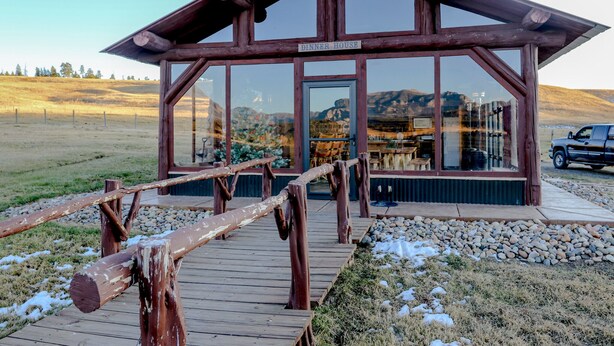 A wooden building labeled "DINNER HOUSE" with a wooden deck leading to it, surrounded by a natural landscape.
