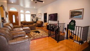 A spacious living room with leather sofas, a large rug, a ceiling fan, and a framed picture on the wall. - Kodiak, Alaska Executive Home  (Kodiak)
