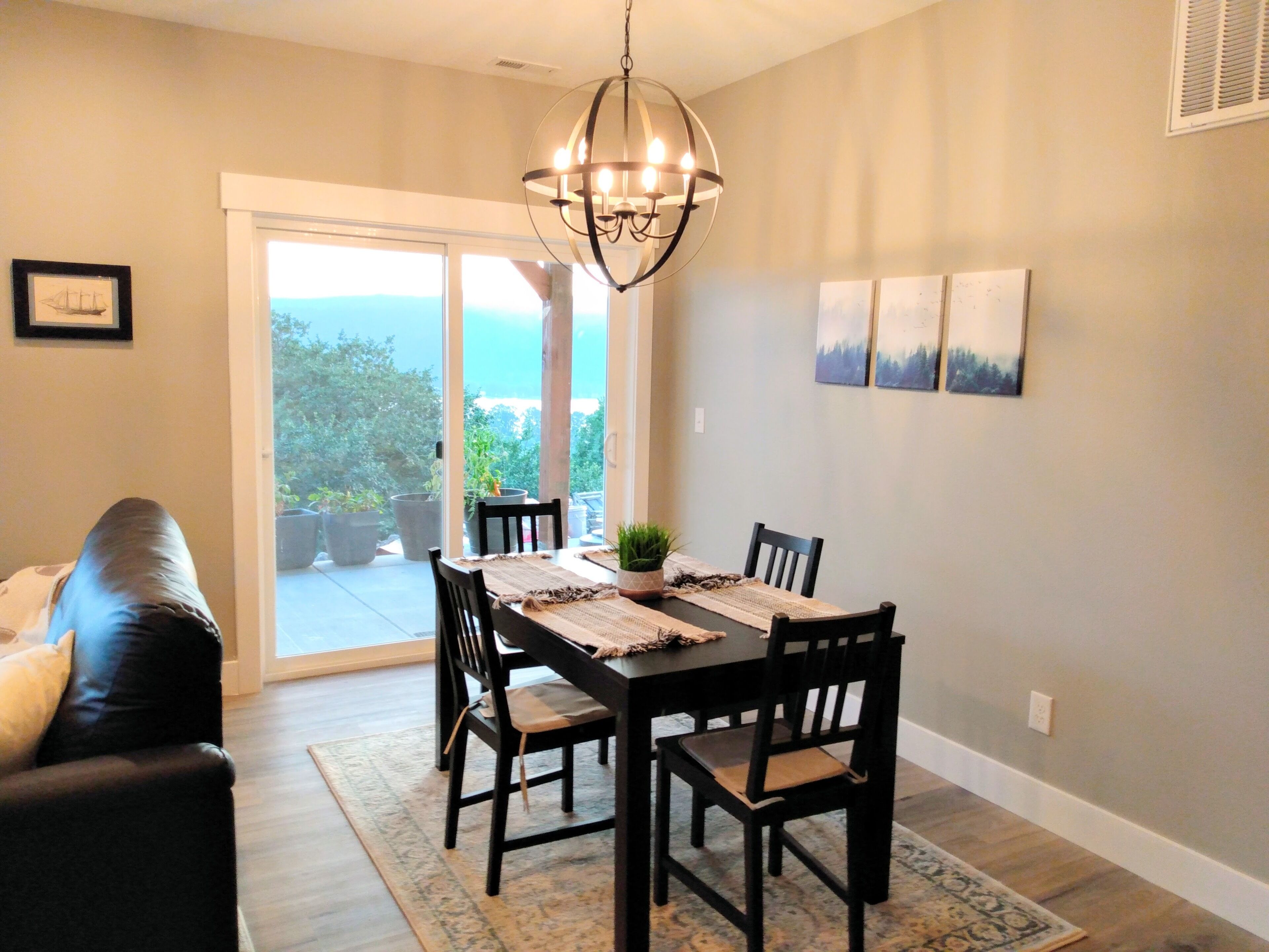 A dining area with a table set for four, surrounded by chairs, a chandelier, and a view through a glass door to the outdoors.