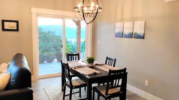 A dining area with a table set for four, surrounded by chairs, a chandelier, and a view through a glass door to the outdoors.