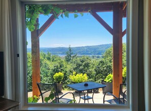 A patio with a table and chairs, a pergola with climbing plants, and a scenic view of a lake and forest. - Gallery of Picture Windows, River & Garden Views, Living landscapes :Kalama Oaks (Kelso)