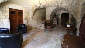 A stone-walled room with a wooden door, a black leather chair, a wooden table, and a chandelier. - La Bastide du Vebron (Grospierres)