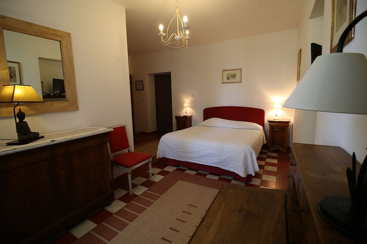 Un dormitorio con cama, una silla, un escritorio, un espejo y una araña.