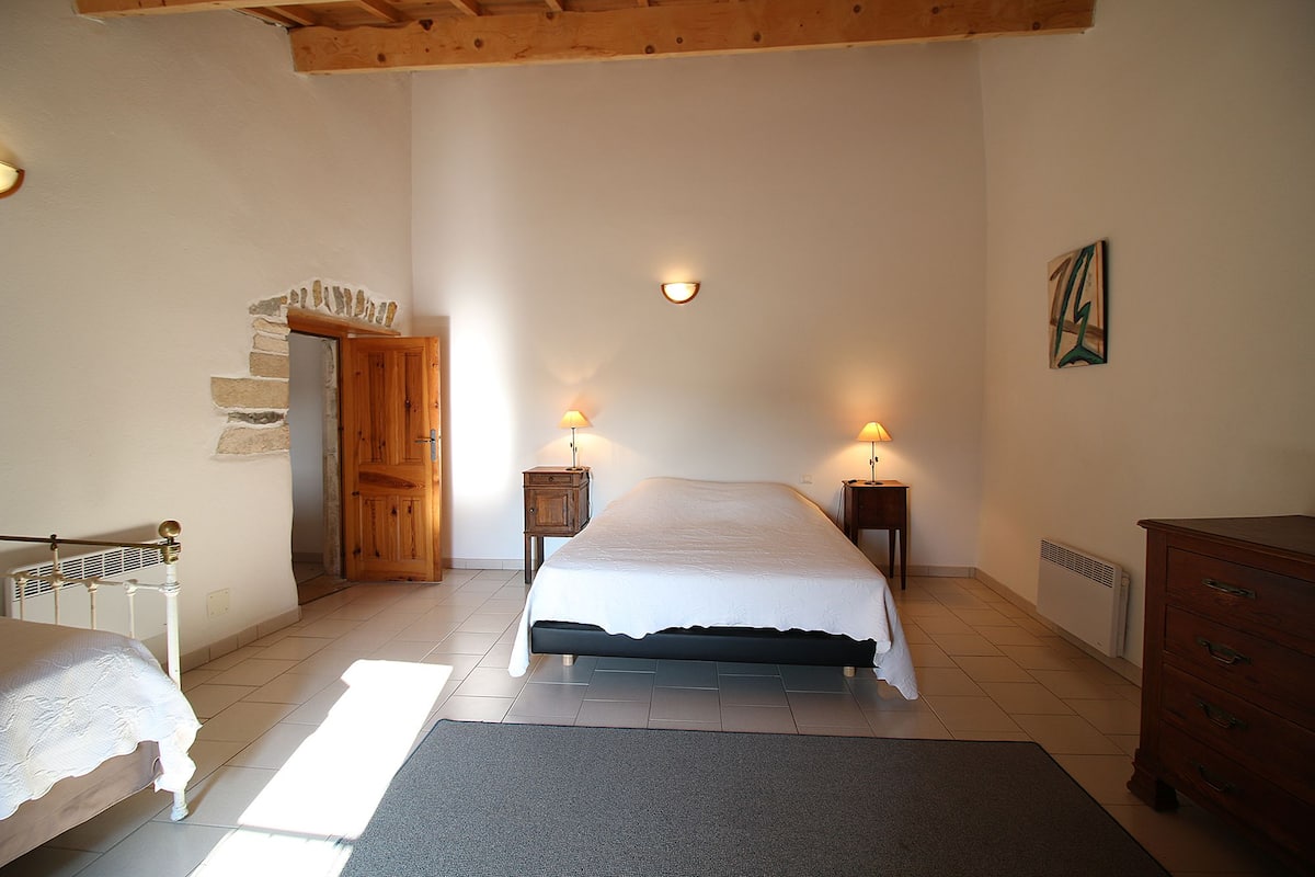 Un dormitorio con cama, mesitas de noche, cómoda, radiador y pared de piedra.