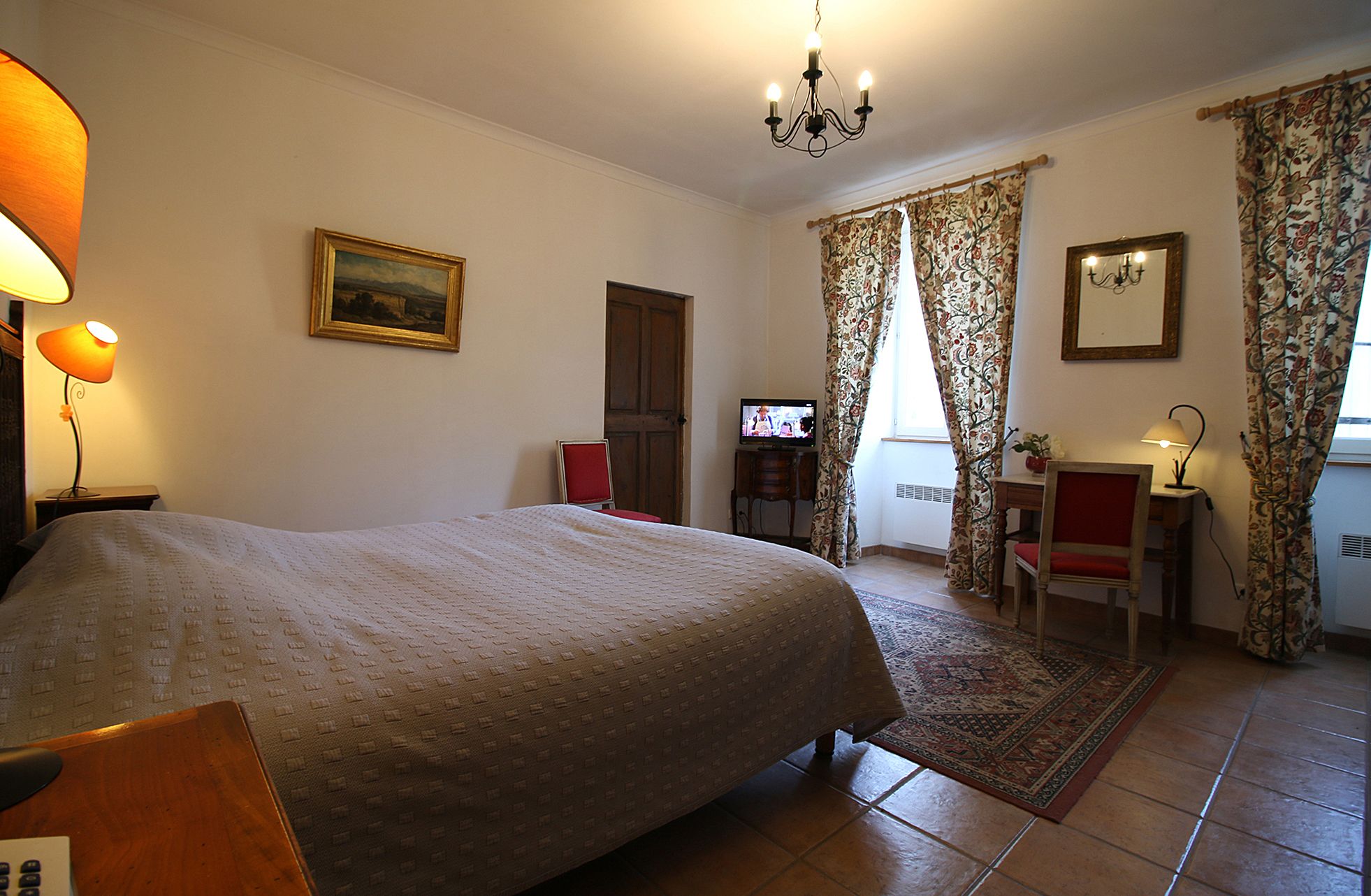 Ein Hotelzimmer mit Bett, Schreibtisch mit Stuhl, Fernseher und einer Kristallleuchter.