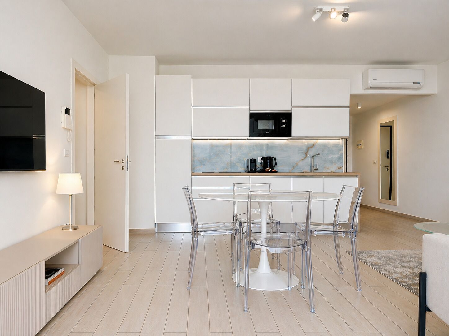 Une cuisine moderne avec des meubles blancs, un micro-ondes noir et une table à manger en verre, assortie de chaises.