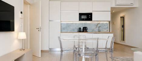 Una cocina moderna con armarios blancos, un microondas negro y una mesa de vidrio con sillas.