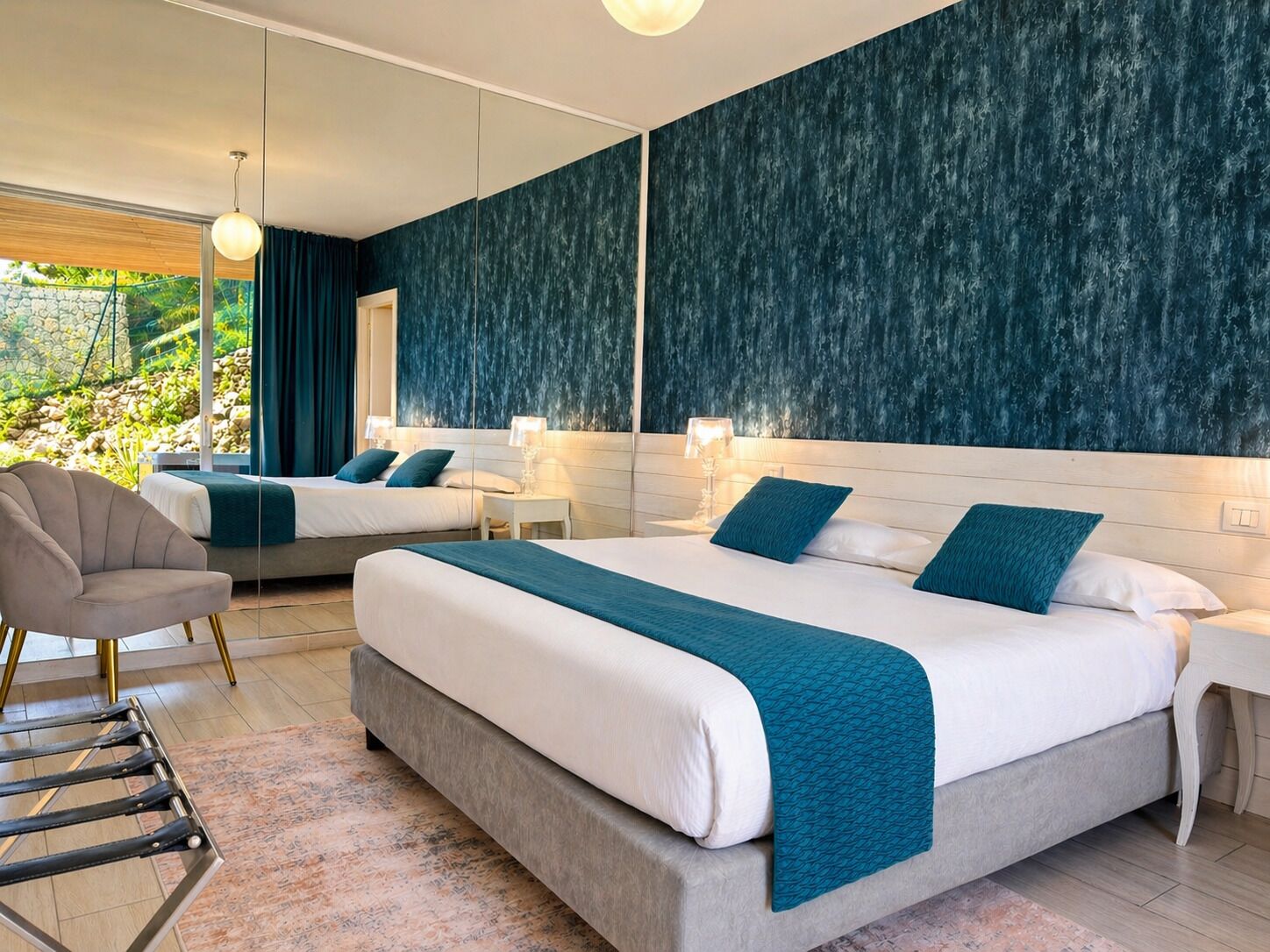 Ett modernt hotellrum med två sängar, en sittgrupp med en fåtölj, ett litet bord och ett stort fönster med utsikt över grönområden.
