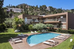 Una villa moderna con piscina, sillones de descanso y un jardín exuberante.