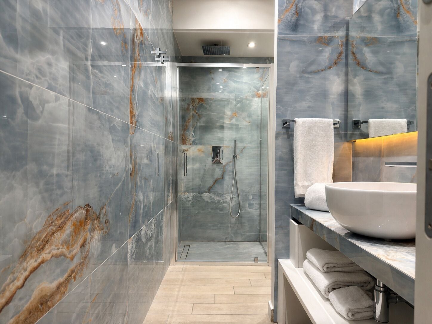 A modern bathroom with a glass-enclosed shower, marble walls, and a large vessel sink.
