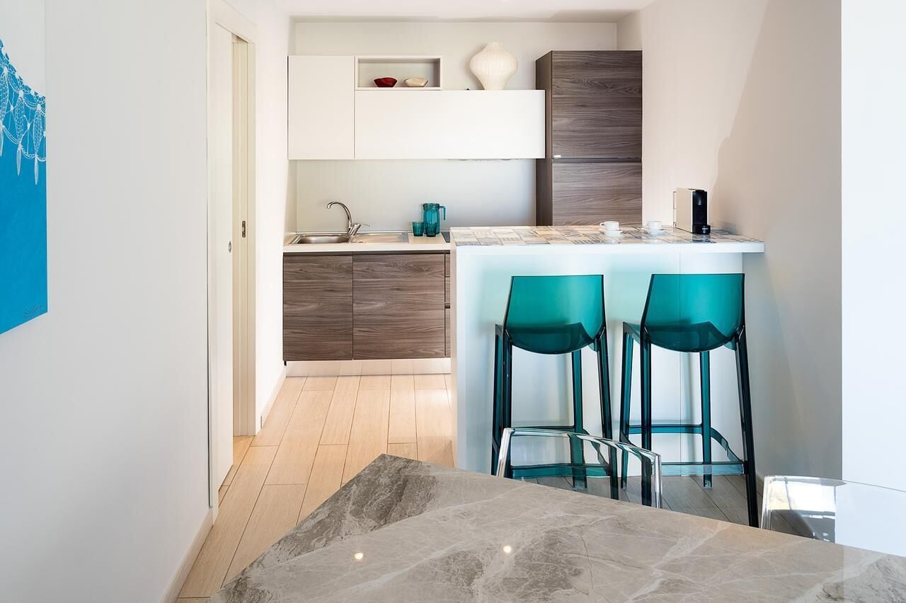 Eine moderne Küche mit Marmorarbeitsplatte, zwei smaragdgrünen Barhocker und Holzschränken.