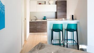 Una cucina moderna con un piano di lavoro in marmo, due sgabelli da bar color petrolio e mobili in legno.