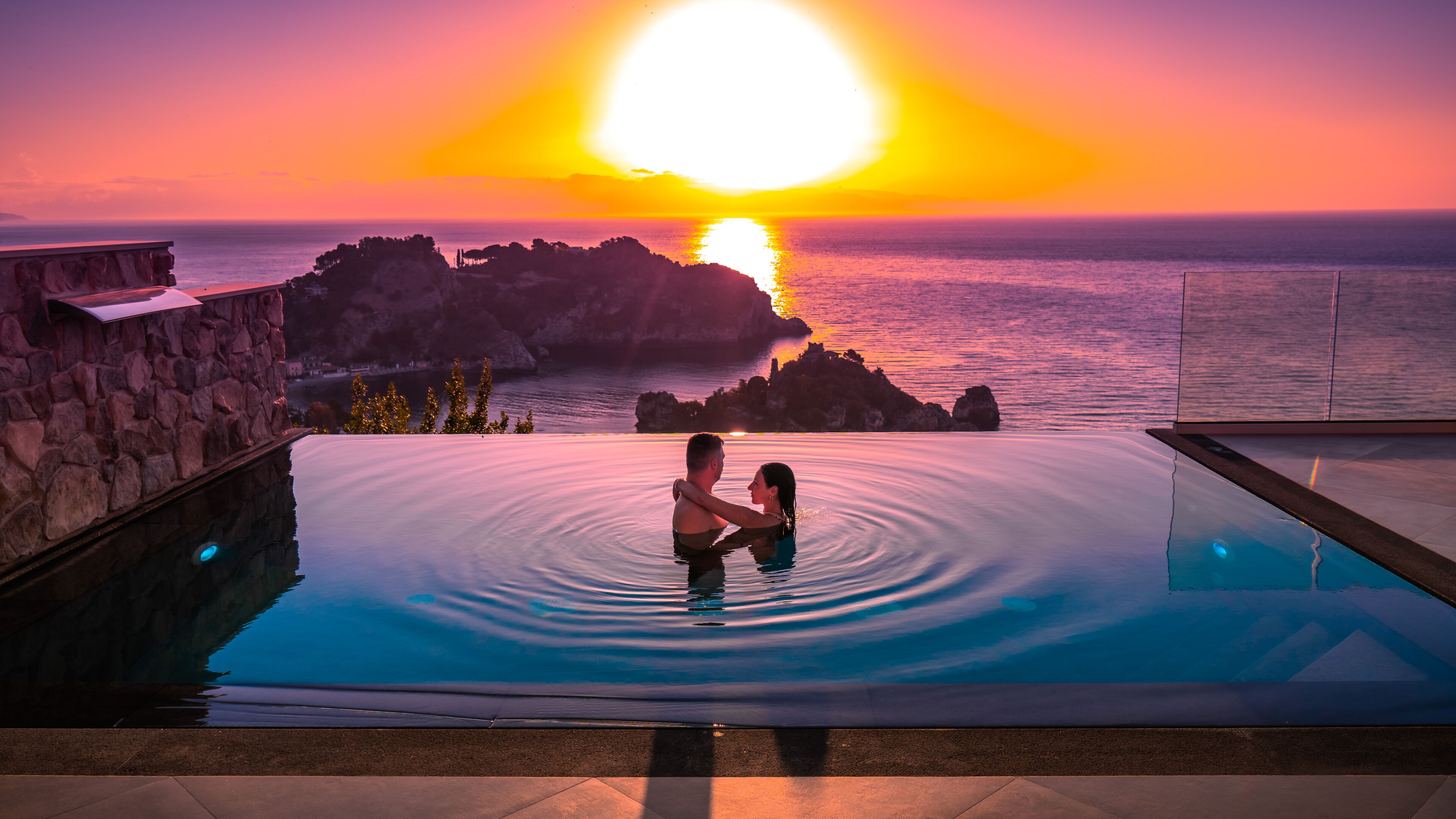 Una pareja en una piscina infinita con vistas al atardecer.