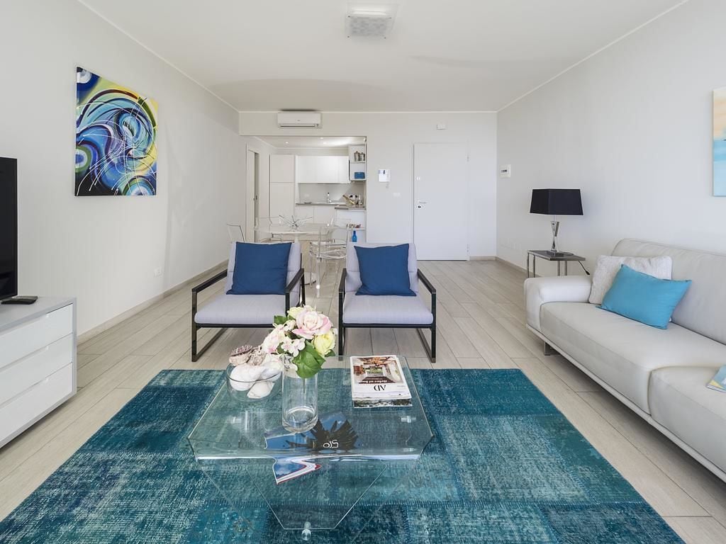A modern living room with a glass coffee table, two armchairs, a sofa, and a TV.