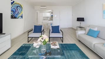 A modern living room with a glass coffee table, two armchairs, a sofa, and a TV.