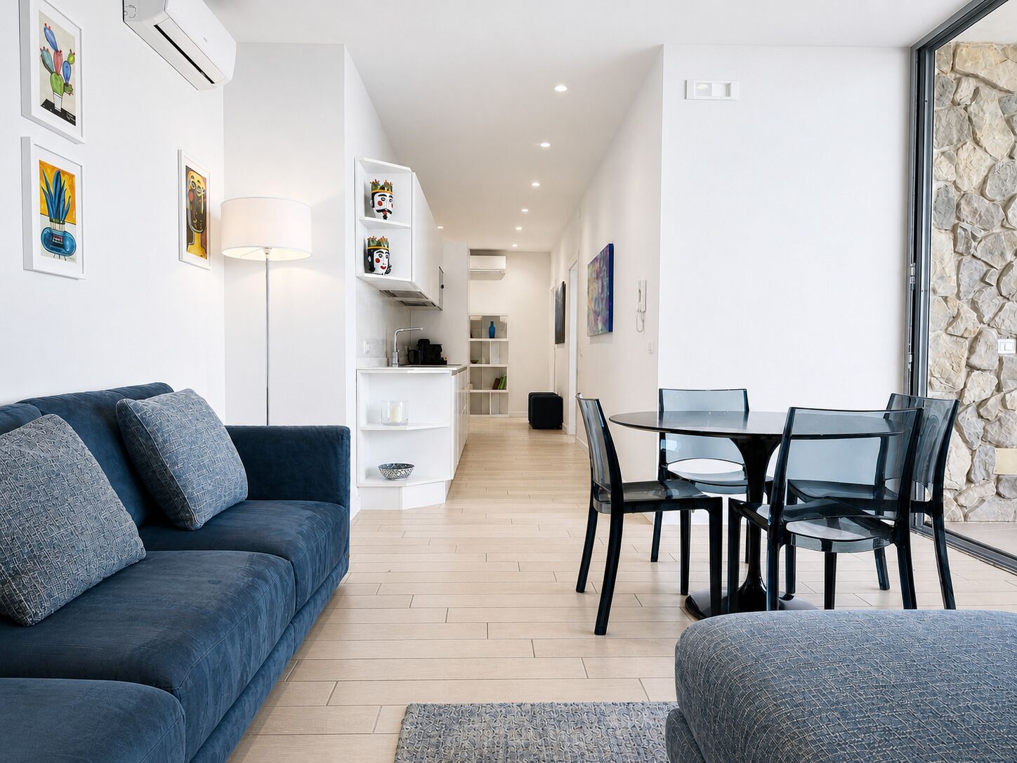 A modern living room with a blue sofa, a dining table with chairs, and a kitchen area in the background.