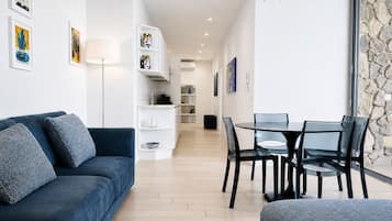 A modern living room with a blue sofa, a dining table with chairs, and a kitchen area in the background.