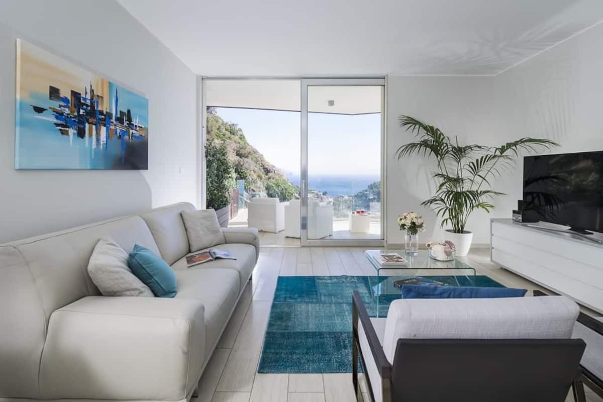 Una sala de estar moderna con un sofá, una mesa de centro y un televisor. Hay un ventanal con vistas al exterior.