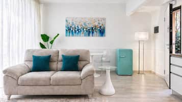 Un salon moderne avec un canapé beige, une table basse en verre, un meuble turquoise et un tableau accroché au mur.