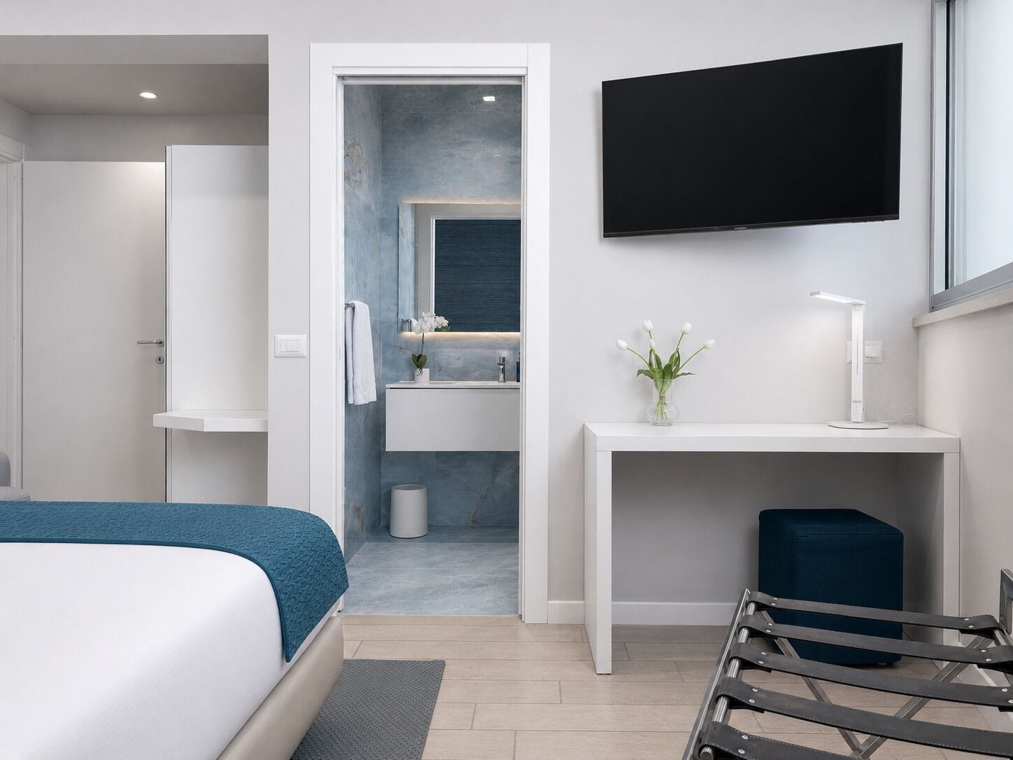 A modern hotel room with a bed, a desk, a TV, and a bathroom visible through an open door.