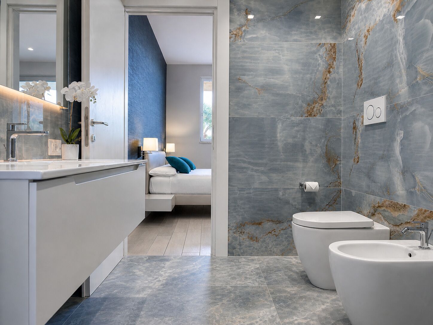 Un baño moderno con pared de mármol, inodoro blanco, bidé y lavabo.