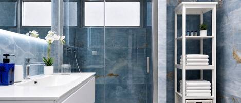 A modern bathroom with a glass shower enclosure, a white vanity with a sink, and a white shelving unit with towels.