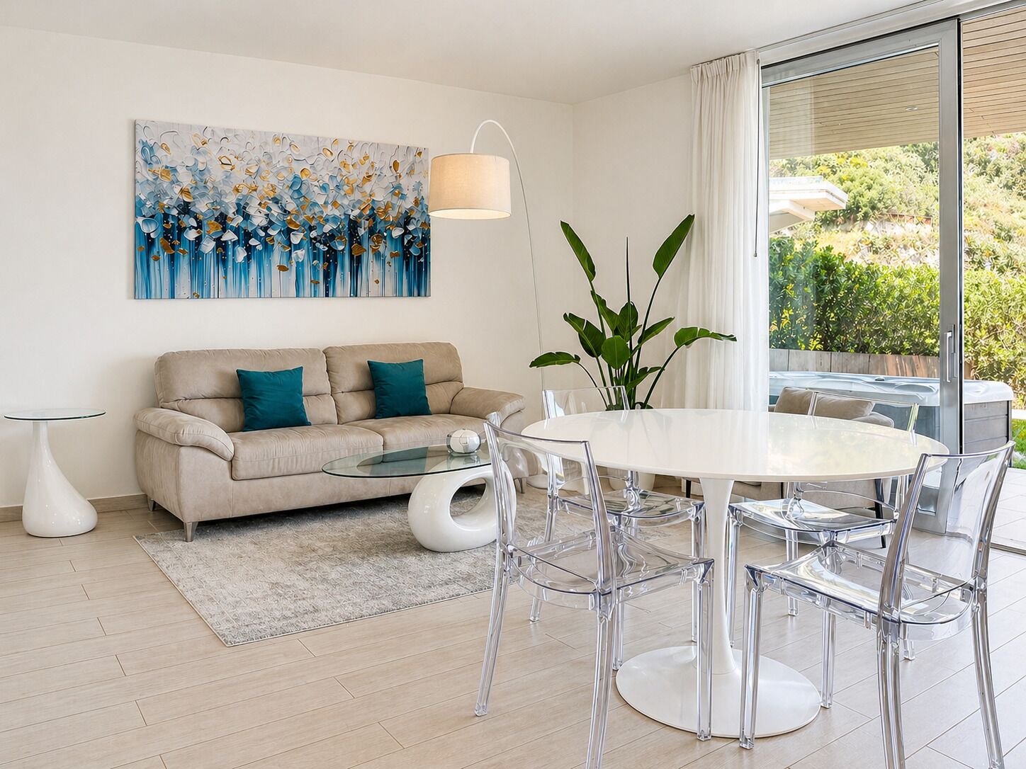 Een moderne woonkamer met een bank, salontafel en transparante stoelen. Aan de muur hangt een schilderij en er is een groot raam met uitzicht op groen.