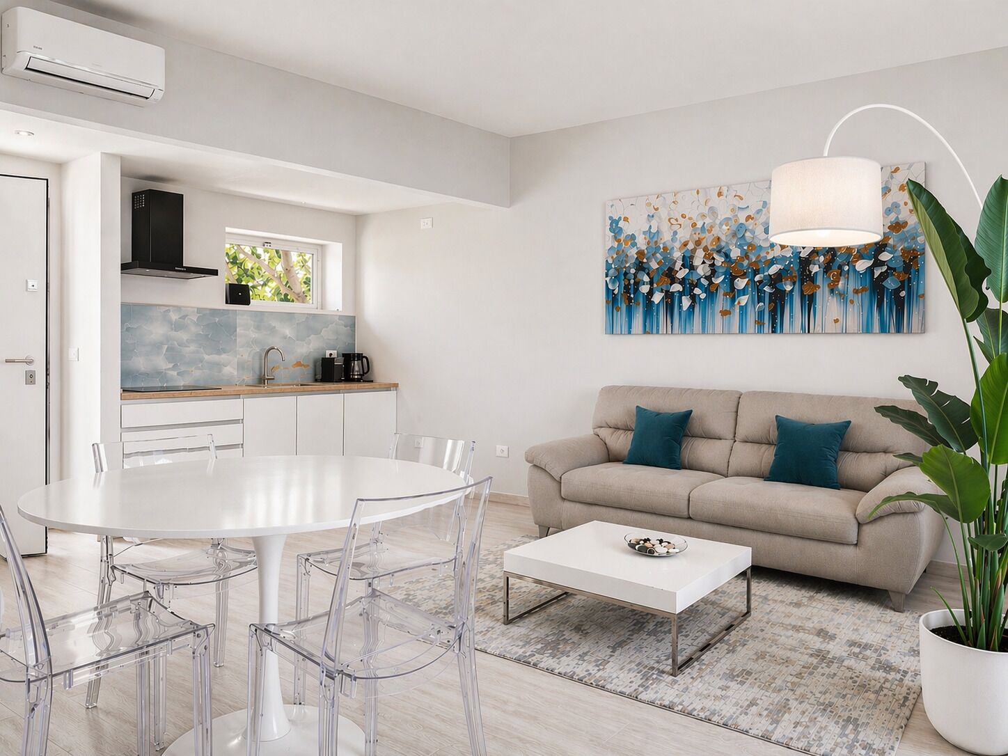 A modern living room with a white dining table, clear chairs, a beige sofa with teal cushions, a coffee table, and a large abstract painting on the wall.