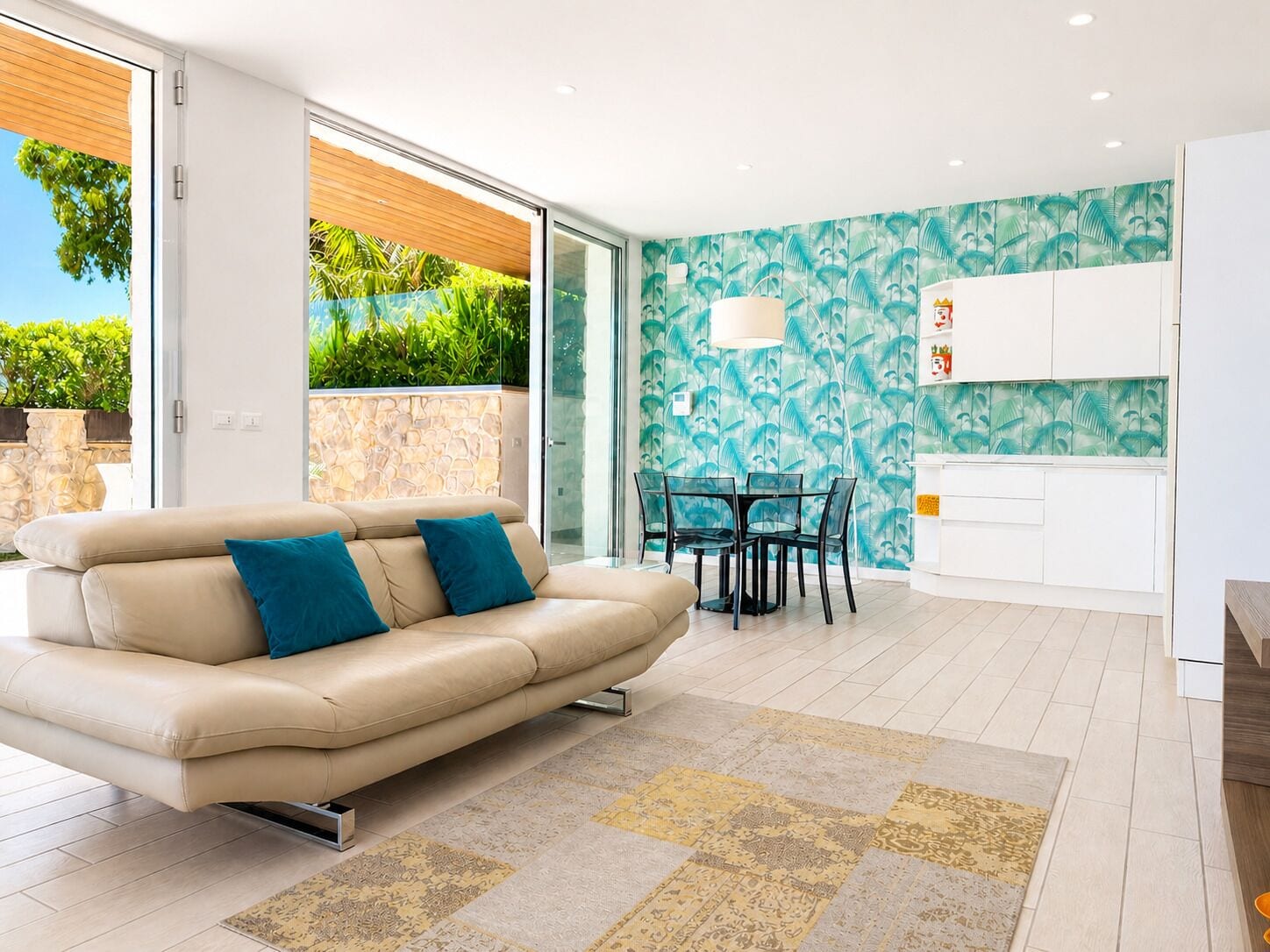 Un salon moderne comprenant un canapé, une table à manger avec des chaises, un coin cuisine et une vue sur la verdure à l’extérieur.