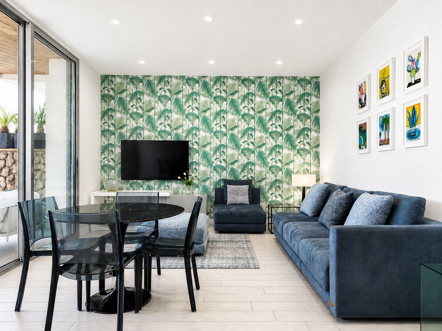 A modern living room with a glass dining table, a sofa, and a TV mounted on the wall.
