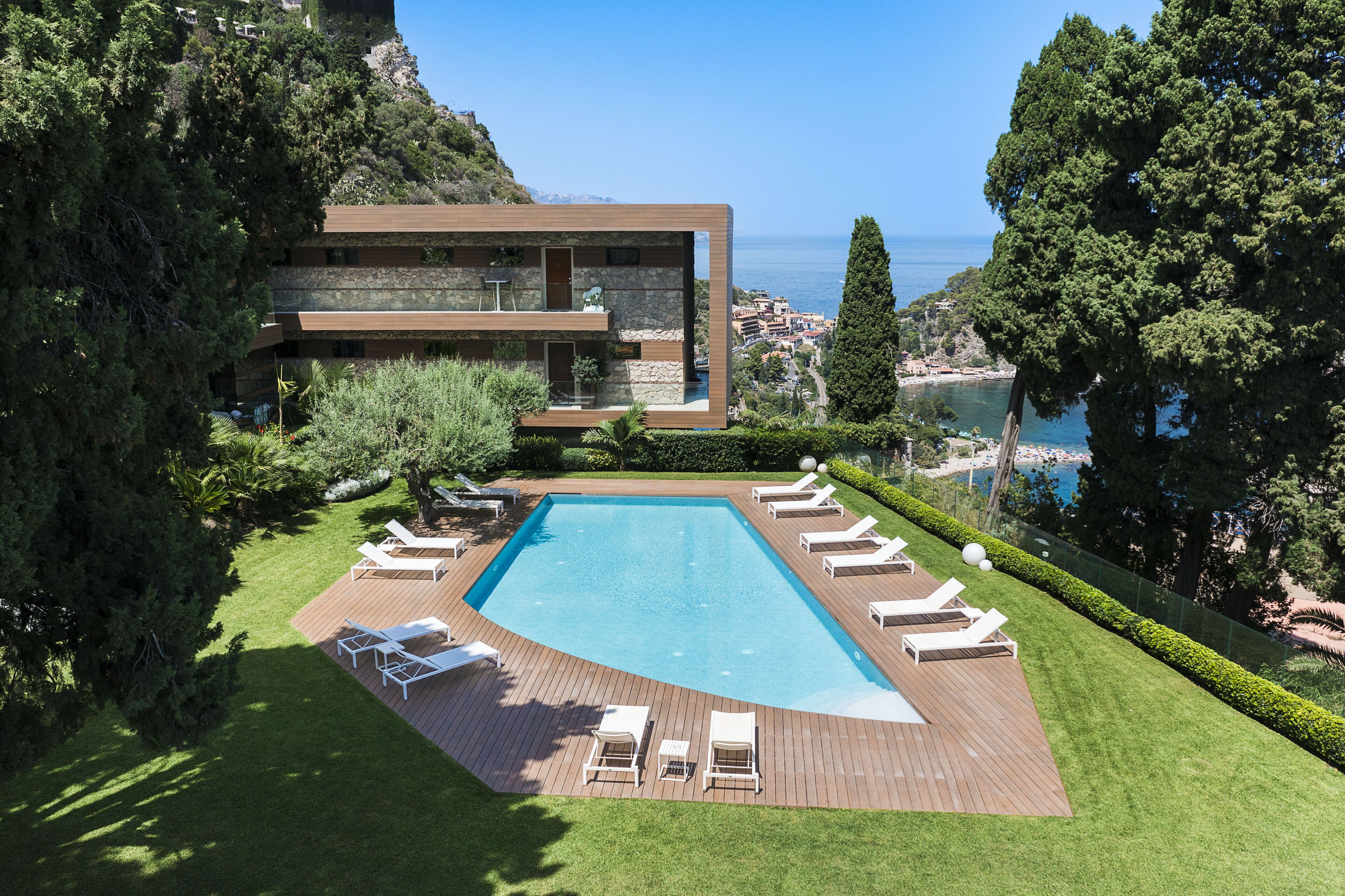 Une villa moderne dotée d’une piscine, de chaises longues et offrant une vue sur la mer.