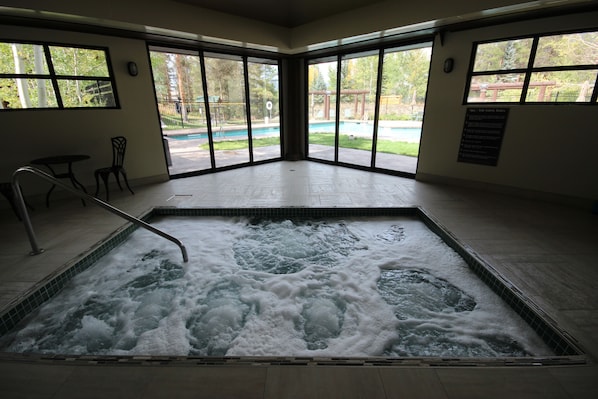A spa area with a hot tub, large windows, and a view of a pool and garden. - Soda Spring II 1927 (Keystone)