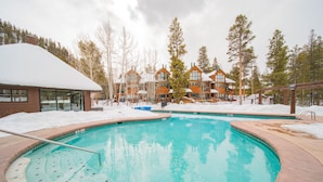 Un espace piscine avec un jacuzzi, entouré de bâtiments et d’un sol recouvert de neige.
