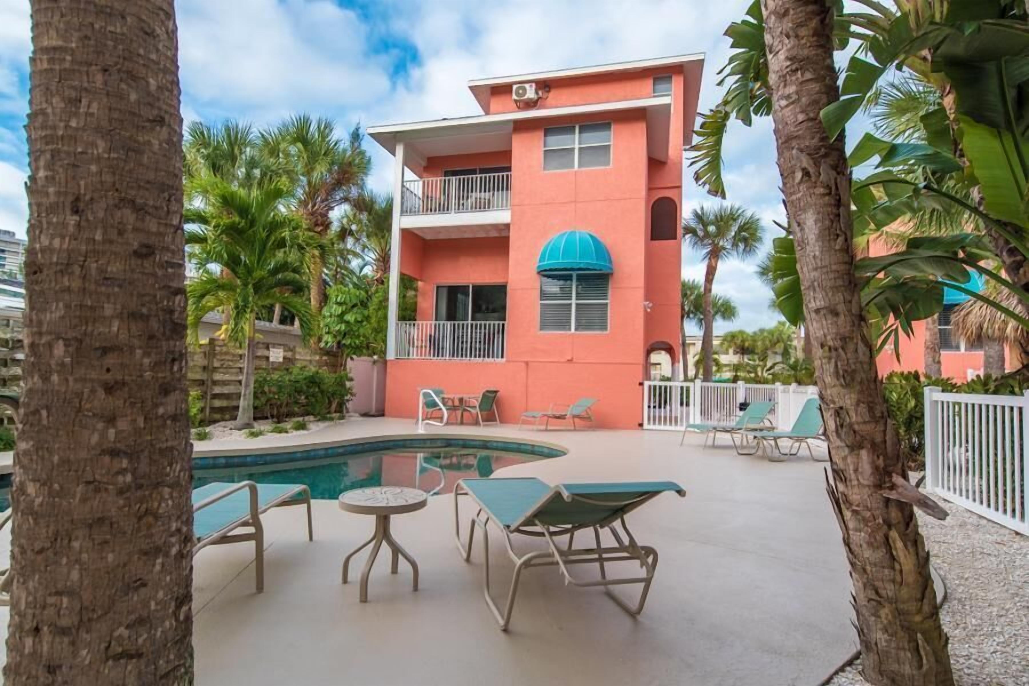 A two-story building with a pool area, including lounge chairs and a small table.