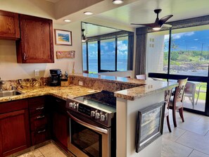 A kitchen with granite countertops, wooden cabinets, a built-in oven, and a large window offering a view of the ocean.