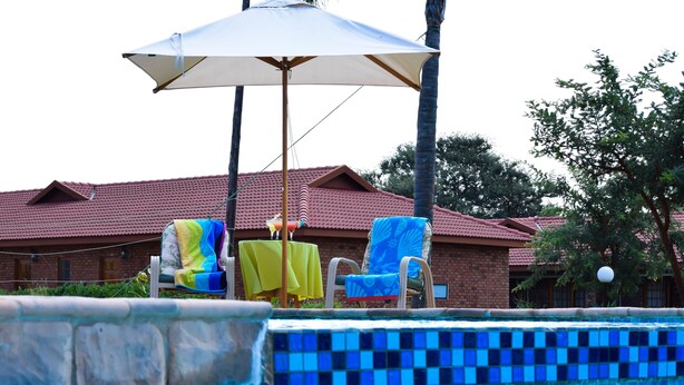 A swimming pool with blue mosaic tiles, two lounge chairs with yellow and blue covers, and a white umbrella. - Zororo lodge (Polokwane)