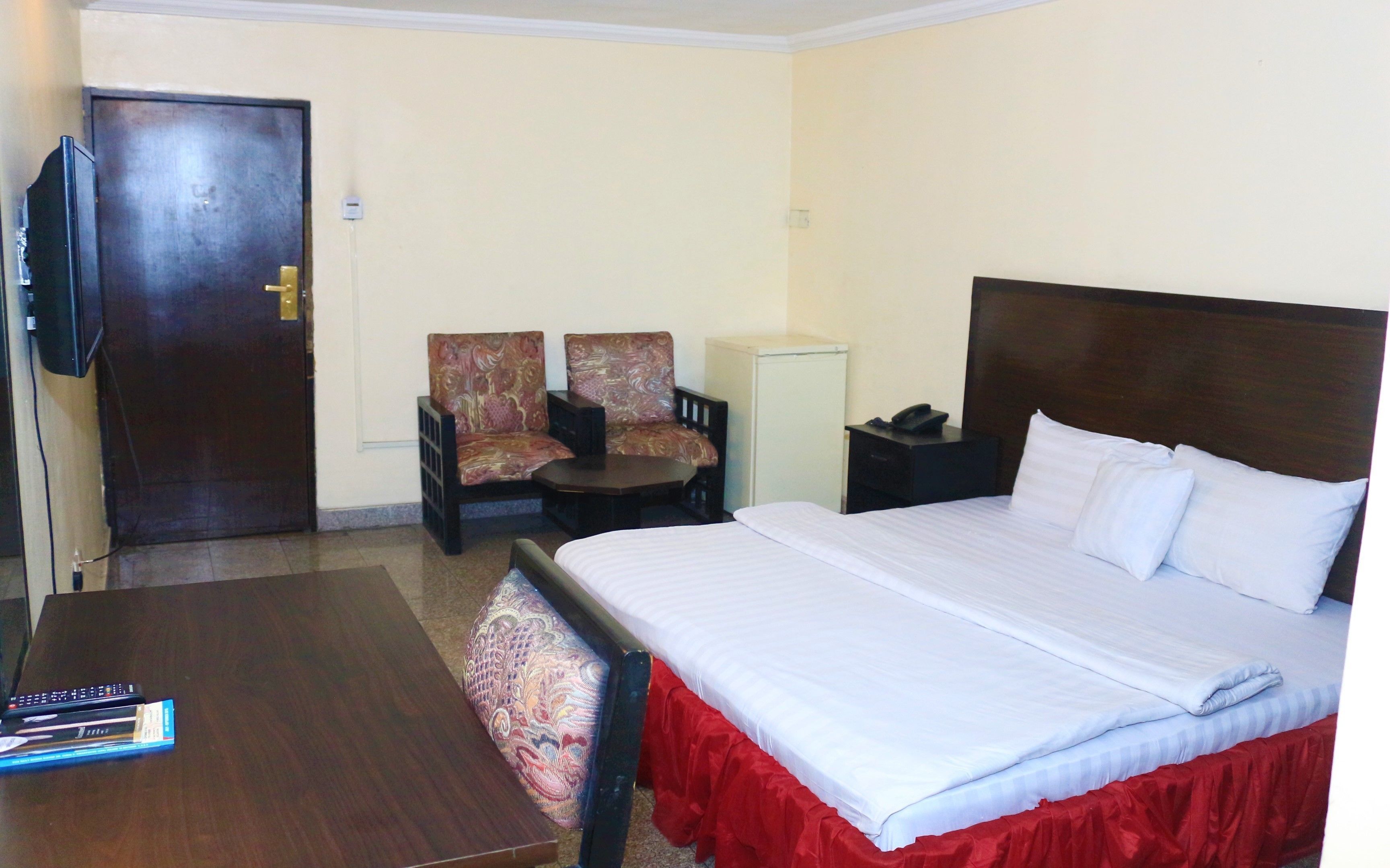 A hotel room with a bed, a desk, two chairs, a television, and a small cabinet.