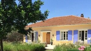 Ein zweigeschossiges Haus mit einem Ziegeldach, einer Veranda und einem gepflegten Garten mit verschiedenen Pflanzen und Blumen.