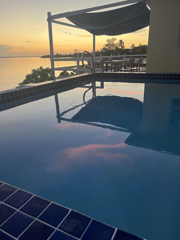 A swimming pool with a view of the sea at sunset. - Beachfront Water's Edge Cottage with pool (newly renovated) (Spanish Wells)