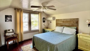A bedroom with a bed, a ceiling fan, a nightstand, a chair, and a window. - Rustic Farmhouse Retreat (McCook)