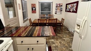 A compact kitchen with a dining table, chairs, a refrigerator, and a stove. - Rustic Farmhouse Retreat (McCook)