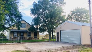 A two-story house with a porch, a fenced yard, and a garage. - Rustic Farmhouse Retreat (McCook)