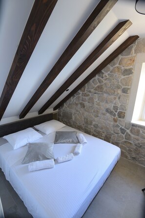 A bedroom with a stone wall, a wooden ceiling, and a bed with white bedding. - Perfect Beachfront Holiday In a Secluded Traditional Stone House With Pool (Mimice)